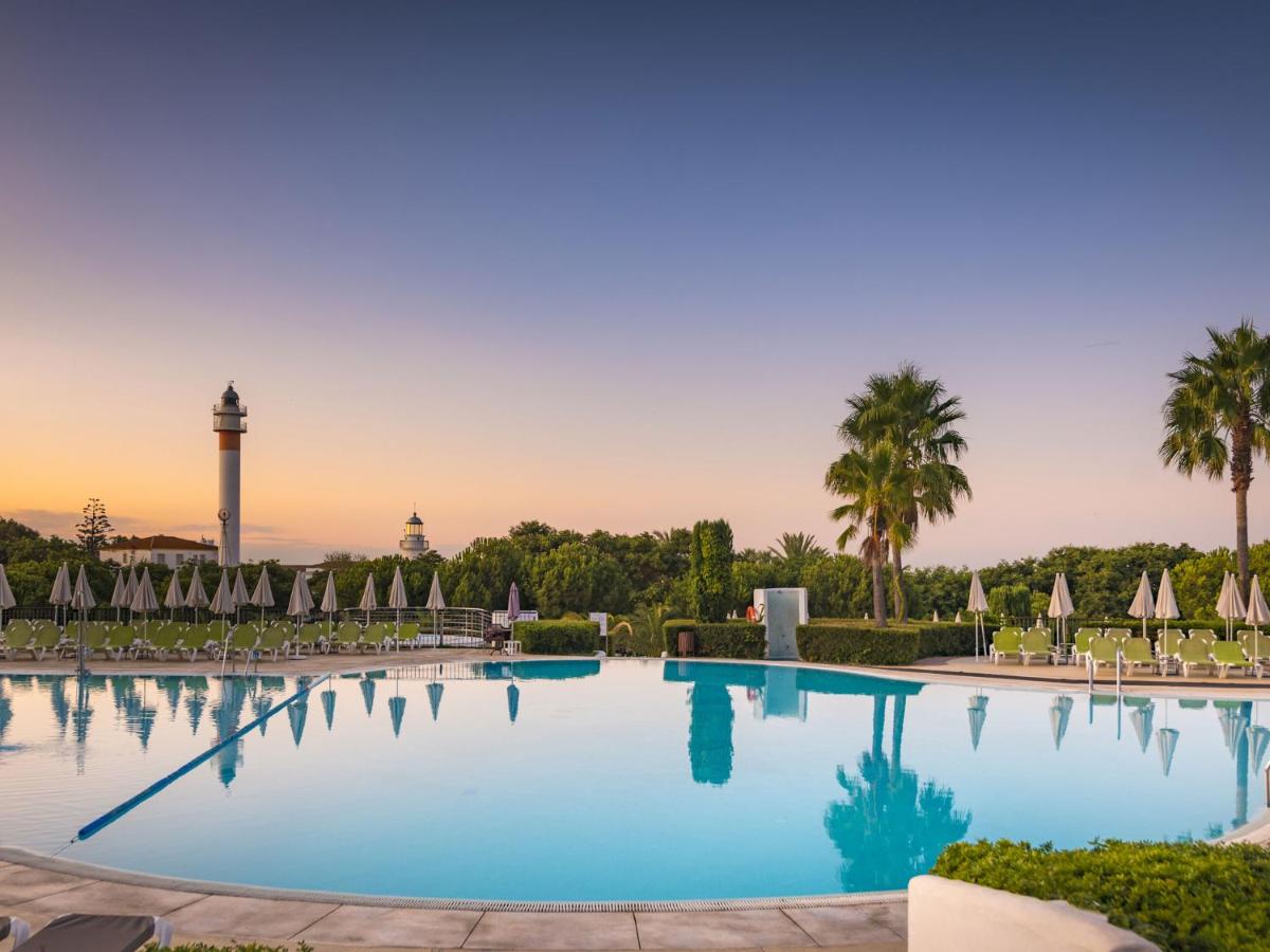 una gran piscina con sombrillas y una torre de reloj. en Hotel Fuerte El Rompido, en El Rompido
