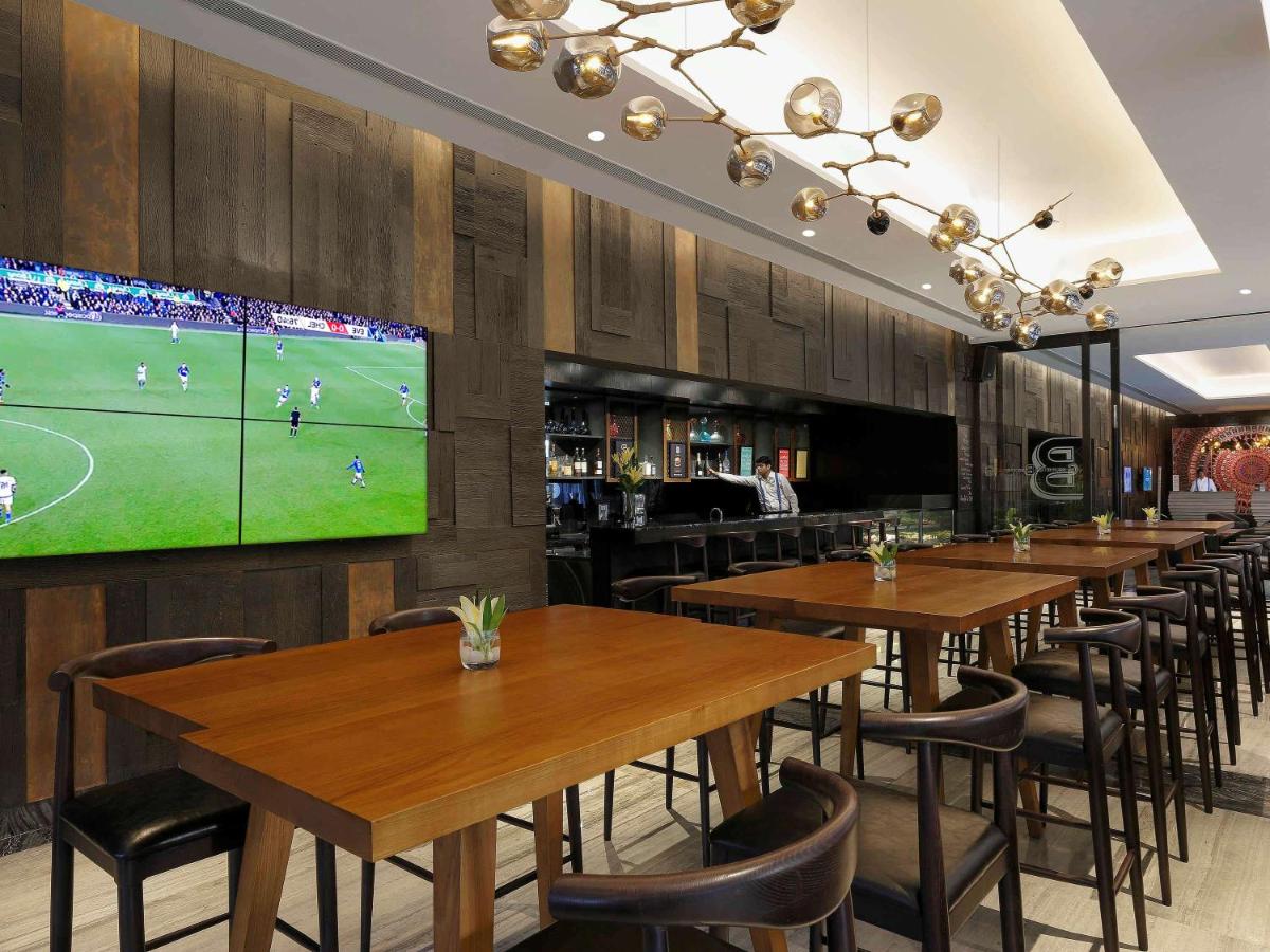 a restaurant with wooden tables and a large tv at Novotel Chennai Chamiers Road in Chennai