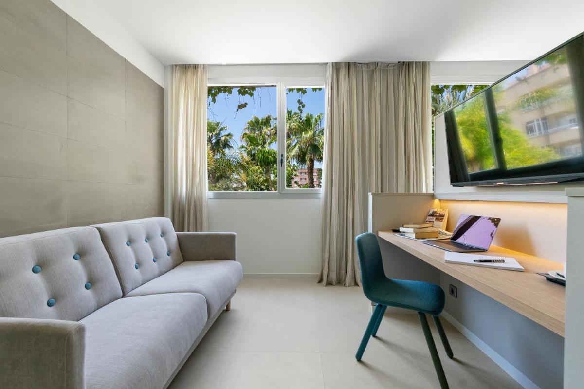 Una sala de estar con un sofá y un escritorio con una computadora portátil. en Hotel Areca, en Torrellano