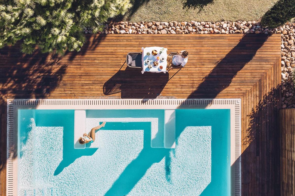 Un hombre sentado en una silla junto a una piscina. en Las Gaviotas Suites Hotel & Spa, en Playa de Muro