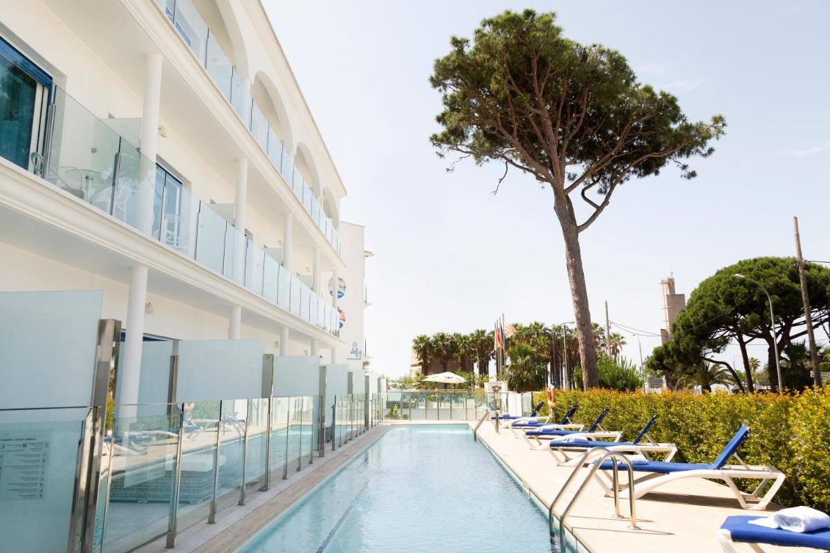 una piscina junto a un edificio con sillas y un árbol en Masd Mediterraneo Hotel Apartamentos Spa, en Castelldefels