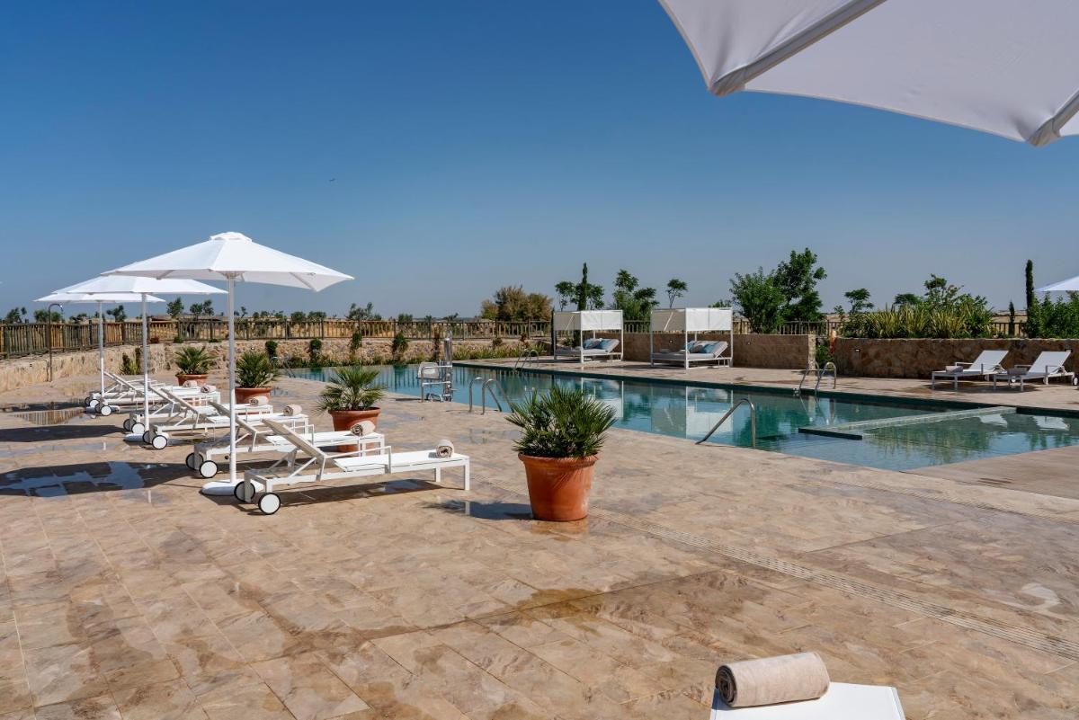Una piscina con tumbonas y sombrillas en un resort. en Hospes Palacio de Arenales & Spa, en Cáceres