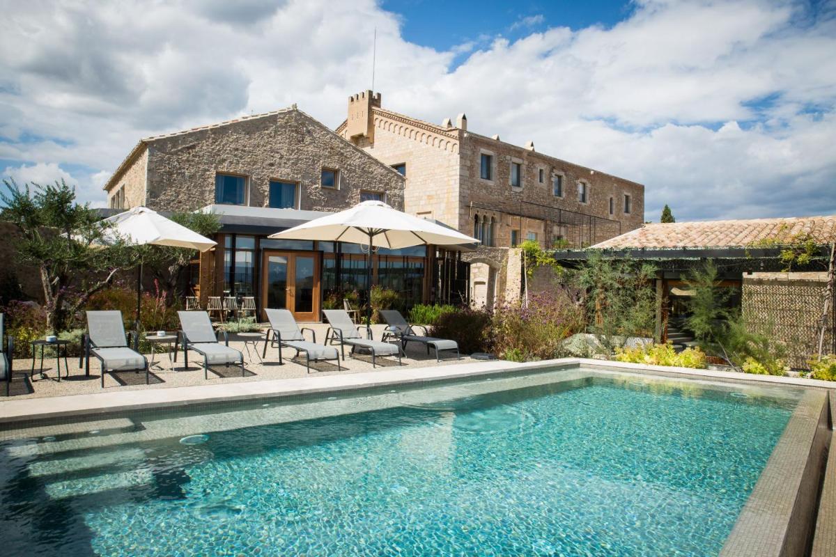 Una piscina con sillas y sombrillas al lado de un edificio. en Hotel Mas Bosch 1526, en Avinyonet de Puigventós Una piscina con sillas y sombrillas al lado de un edificio. en Hotel Mas Bosch 1526, en Avinyonet de Puigventós