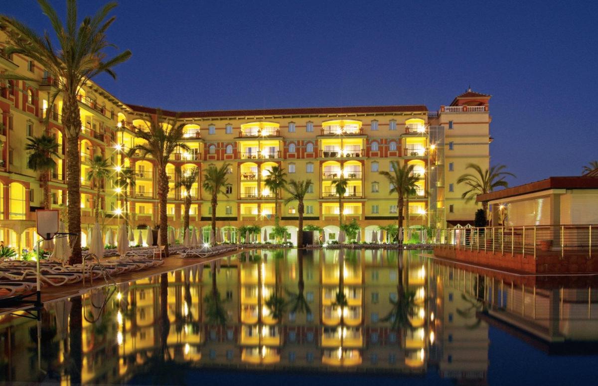 Un edificio con una piscina enfrente por la noche. en Ohtels Islantilla, en Islantilla