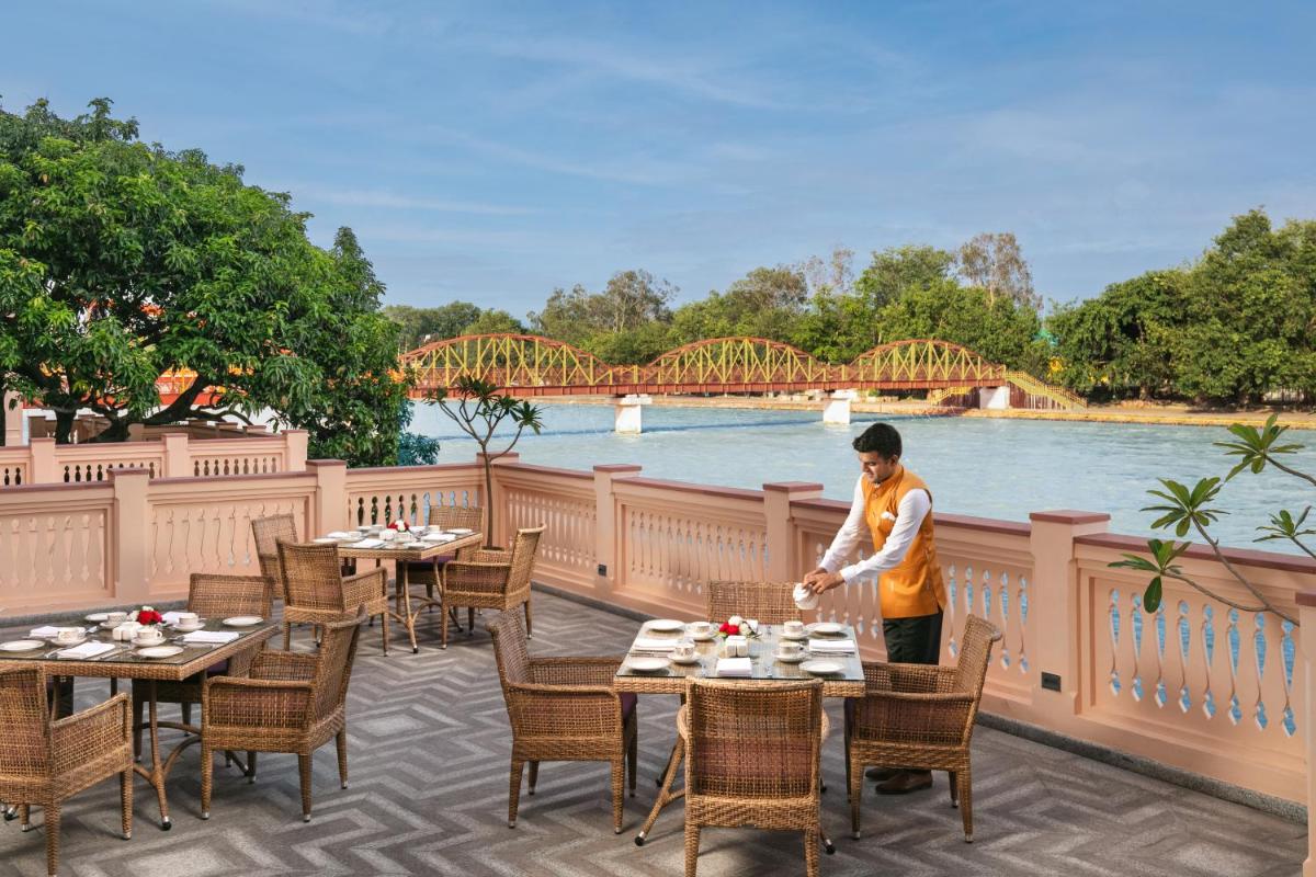 a woman standing on a patio with tables and chairs at Pilibhit House, Haridwar – IHCL SeleQtions in Haridwār