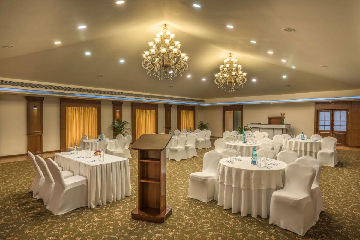 a banquet hall with white tables and chairs and chandeliers at Radisson Goa Candolim in Candolim