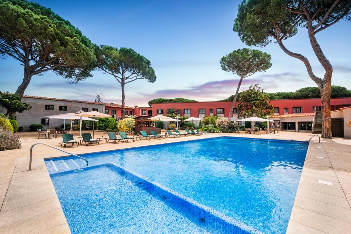 Una piscina con sillas y sombrillas frente a un hotel. en Salles Hotel Aeroport de Girona, en Riudellots de la Selva