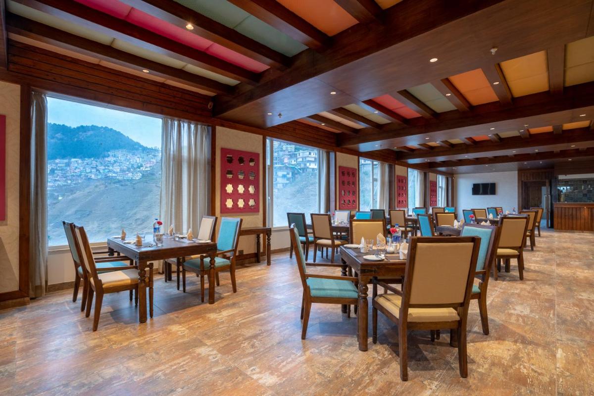 a dining room with tables and chairs and large windows at The Orchid Shimla in Shimla