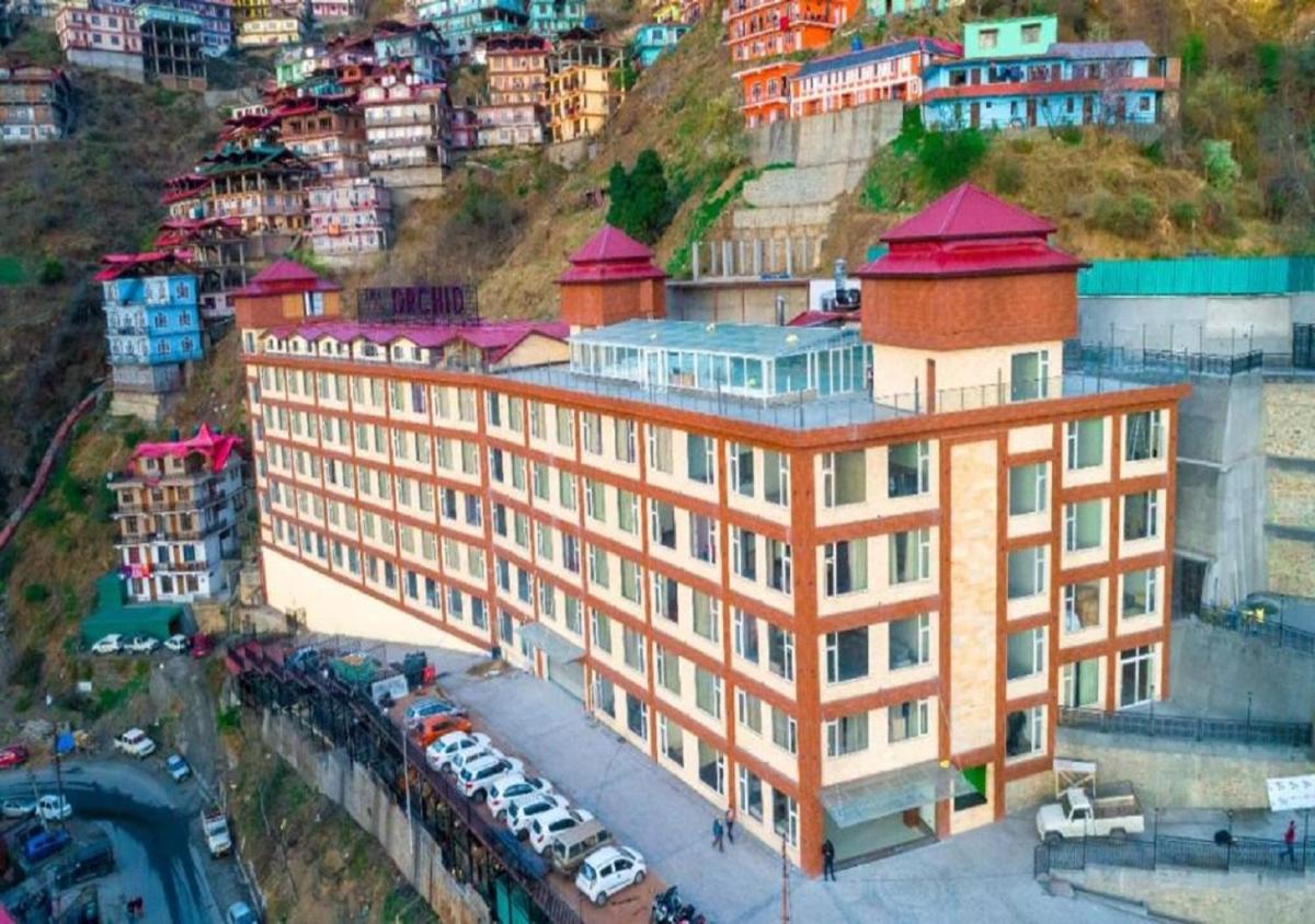 a building on a hill with cars parked in front of it at The Orchid Shimla in Shimla