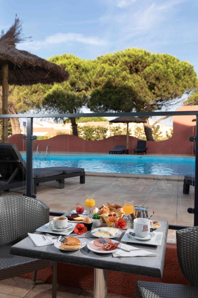 une table avec de la nourriture et une piscine dans l'établissement Relax'Otel & Spa, Le Barcarès, au Barcarès