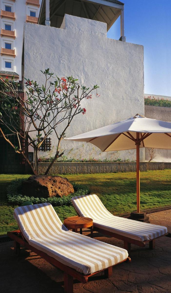 two lounge chairs and an umbrella next to a building at The Leela Mumbai in Mumbai two lounge chairs and an umbrella next to a building at The Leela Mumbai in Mumbai