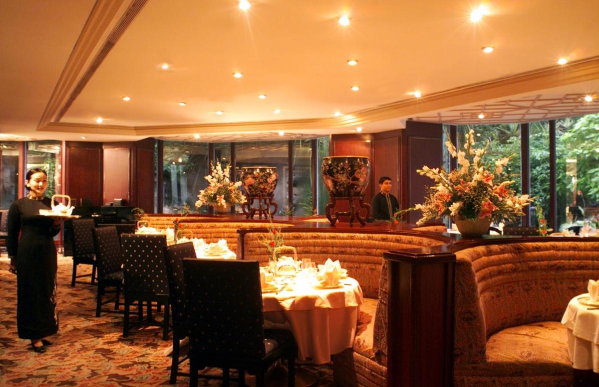 a man standing in a restaurant with tables and chairs at The Leela Mumbai in Mumbai a man standing in a restaurant with tables and chairs at The Leela Mumbai in Mumbai