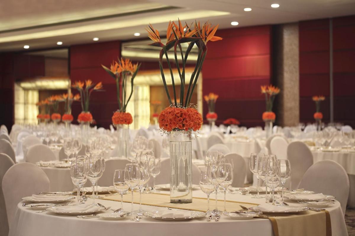 a room filled with tables with white chairs and vases at The Leela Ambience Gurugram Hotel & Residences - The Luxury Urban Sanctuary in Gurgaon
