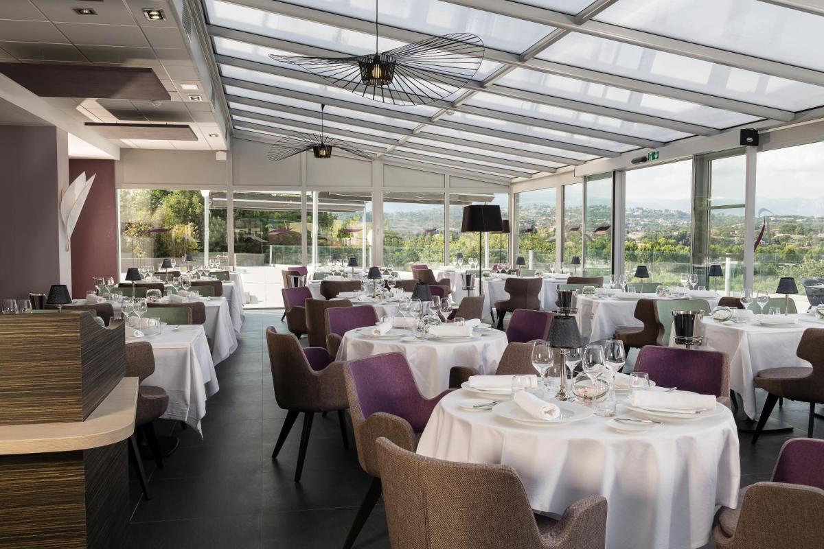 un restaurant avec des tables et des chaises blanches et des fenêtres dans l'établissement Thalazur Antibes - Résidence & Spa, à Antibes