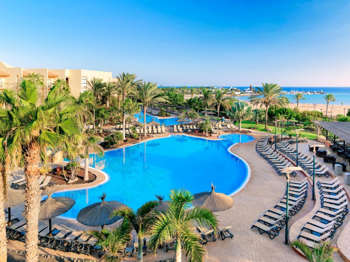 Una vista aérea de una piscina del complejo con sillas y palmeras. en Barceló Fuerteventura Mar, en Caleta de Fuste