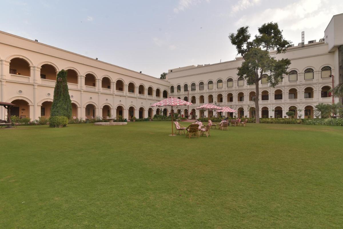 a large building with tables and pink umbrellas in a yard at The Grand Imperial - Heritage Hotel in Agra