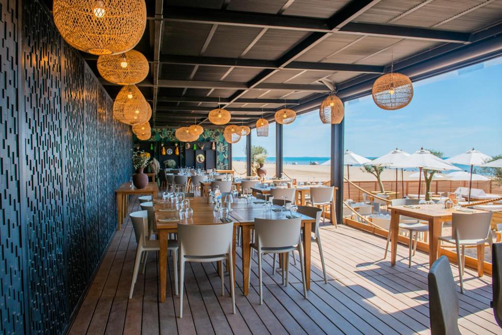un restaurant avec tables et chaises et vue sur la plage dans l'établissement Château L'Hospitalet Wine Resort Beach & Spa, à Narbonne