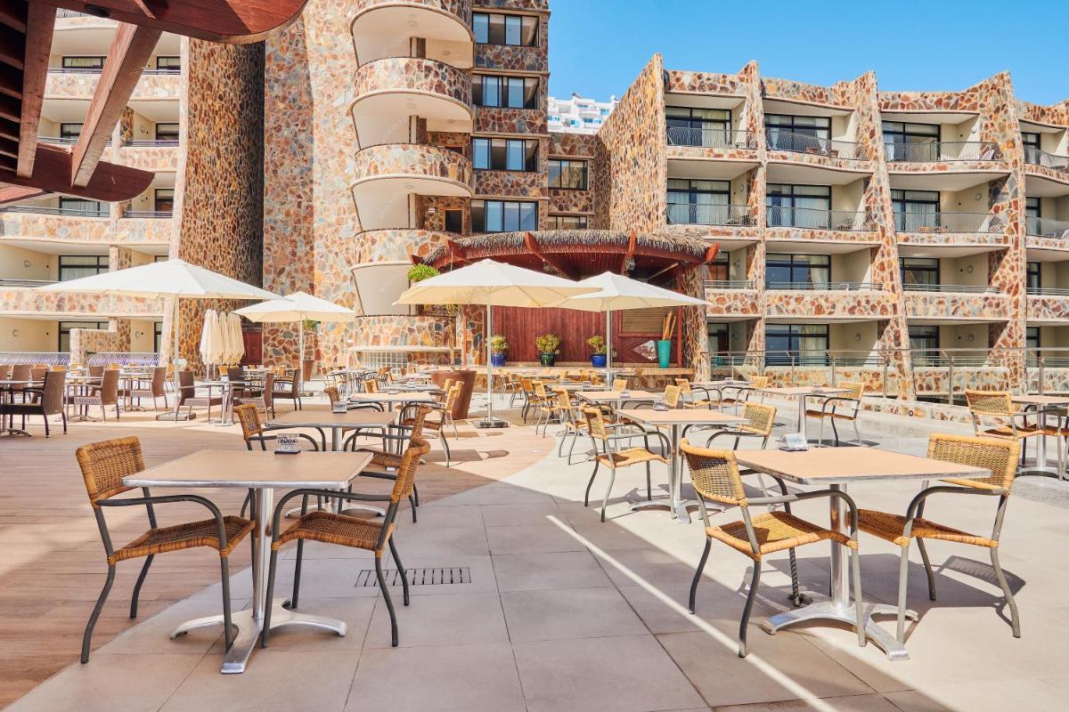 Un patio al aire libre con mesas, sillas y sombrillas. en Gloria Palace Amadores Thalasso & Hotel, en Puerto Rico de Gran Canaria