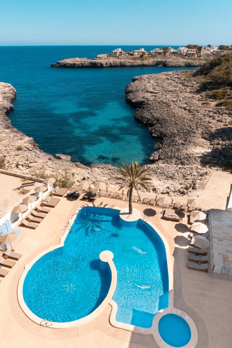 una piscina junto a una playa con el océano en Portomar Apartments - 4-Star Superior Hotel, en Portocolom