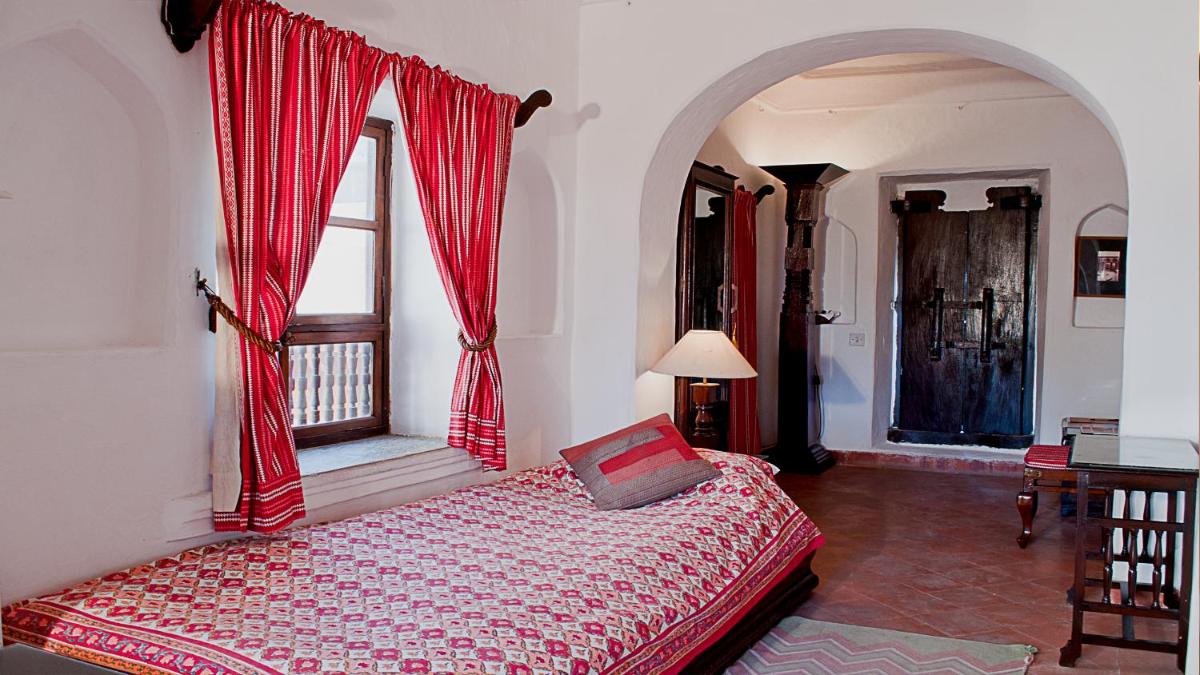 a bedroom with a bed with red curtains and a window at Neemrana Fort-Palace in Neemrana