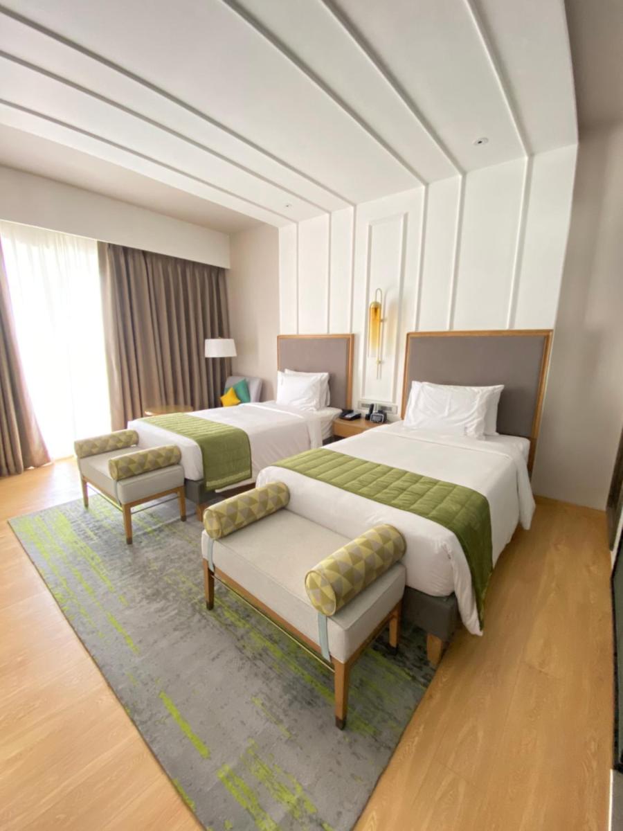 a hotel room with two beds and two chairs at Holiday Inn Goa Candolim in Candolim a hotel room with two beds and two chairs at Holiday Inn Goa Candolim in Candolim