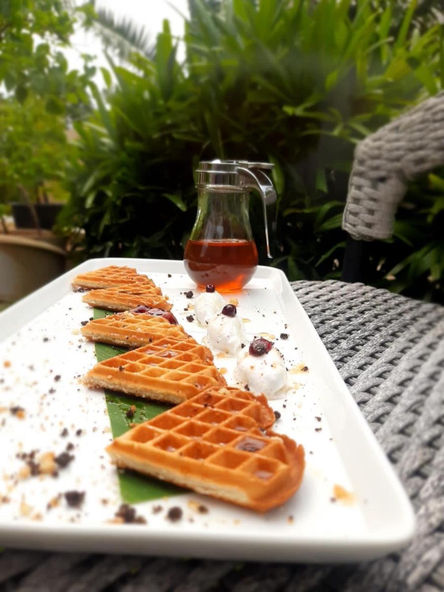 a white plate with waffles and syrup on a table at Holiday Inn Goa Candolim in Candolim a white plate with waffles and syrup on a table at Holiday Inn Goa Candolim in Candolim