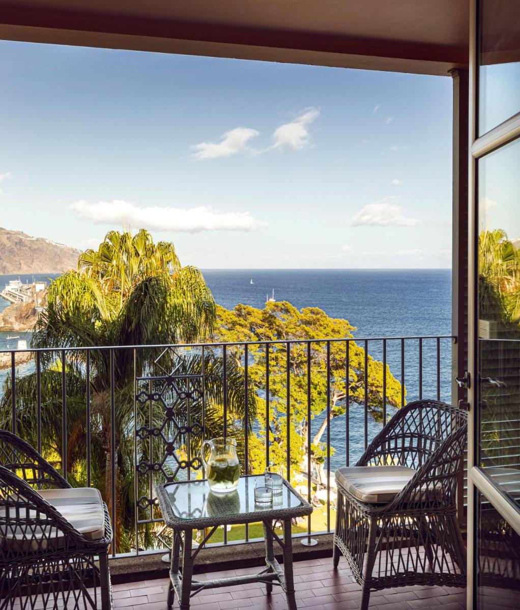 uma varanda com mesa e cadeiras e o oceano em Reid's Palace, A Belmond Hotel, Madeira no Funchal