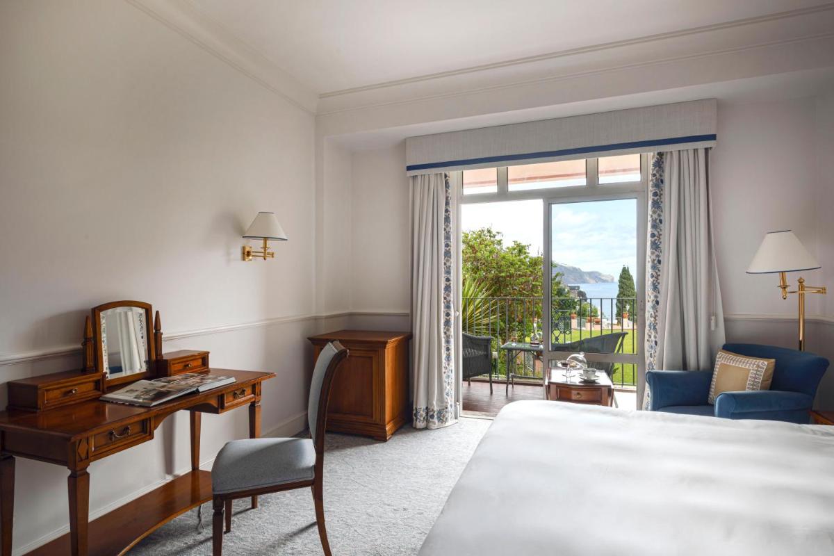 um quarto de hotel com uma cama, uma escrivaninha e uma janela em Reid's Palace, A Belmond Hotel, Madeira no Funchal mais 147 fotografias