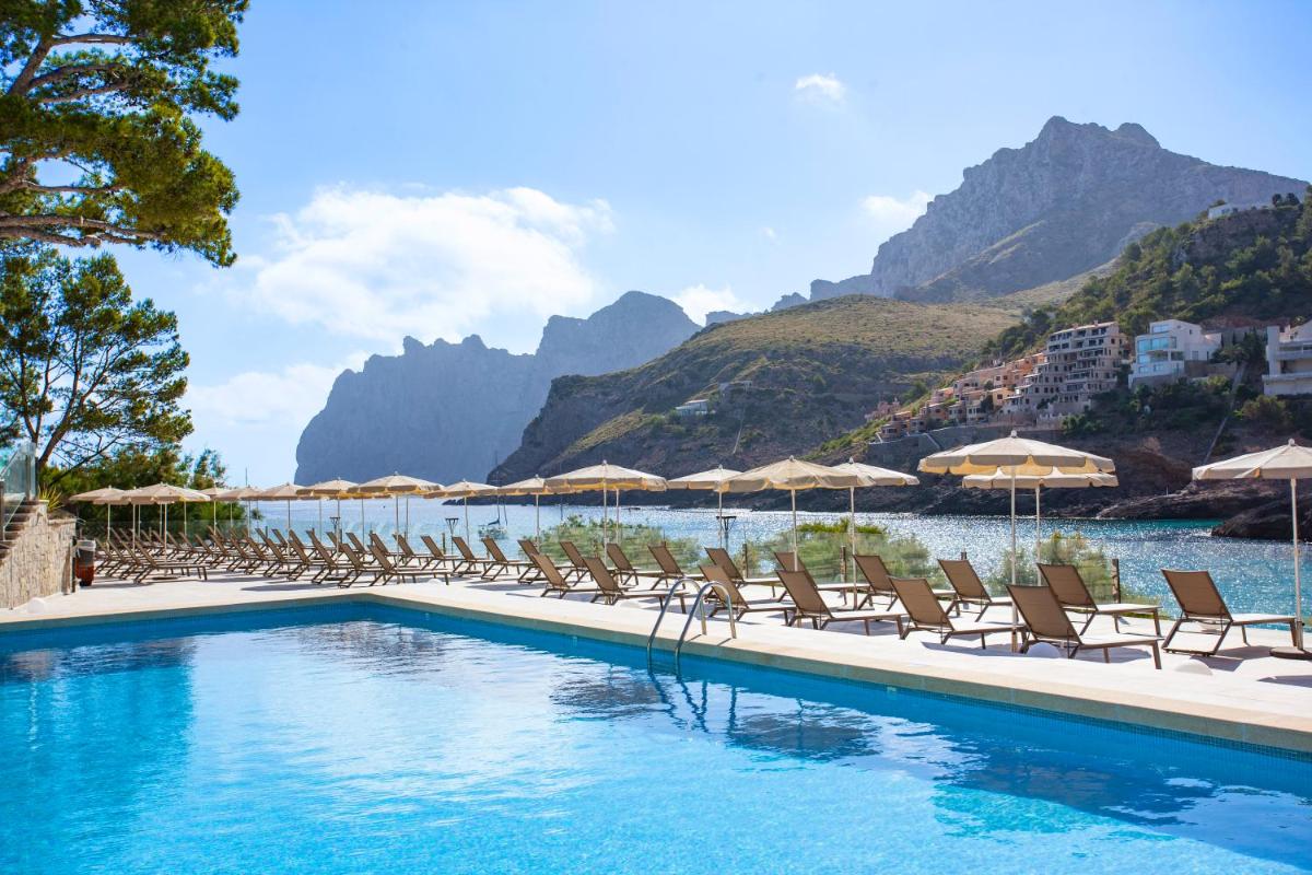 Una piscina con sillas y sombrillas y una montaña. en Grupotel Molins, en Cala de Sant Vicent