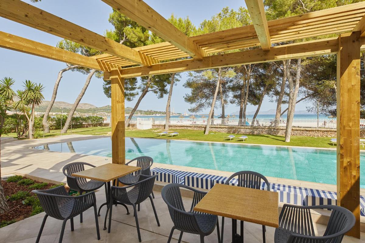 Un patio con mesas y sillas y una piscina. en Sofia Alcudia Beach, en Puerto de Alcudia