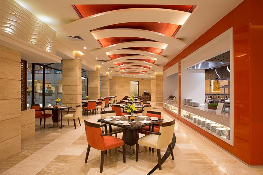a dining room with a table and chairs and a kitchen at The Suryaa New Delhi in New Delhi a dining room with a table and chairs and a kitchen at The Suryaa New Delhi in New Delhi