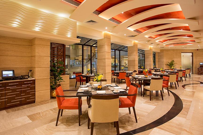 a restaurant with tables and chairs in a room at The Suryaa New Delhi in New Delhi a restaurant with tables and chairs in a room at The Suryaa New Delhi in New Delhi