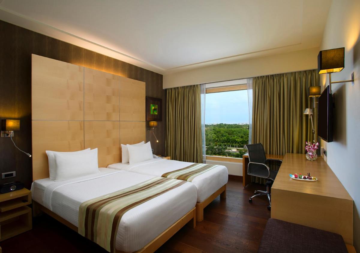a hotel room with a bed and a desk and a window at Novotel Hyderabad Airport in Hyderabad