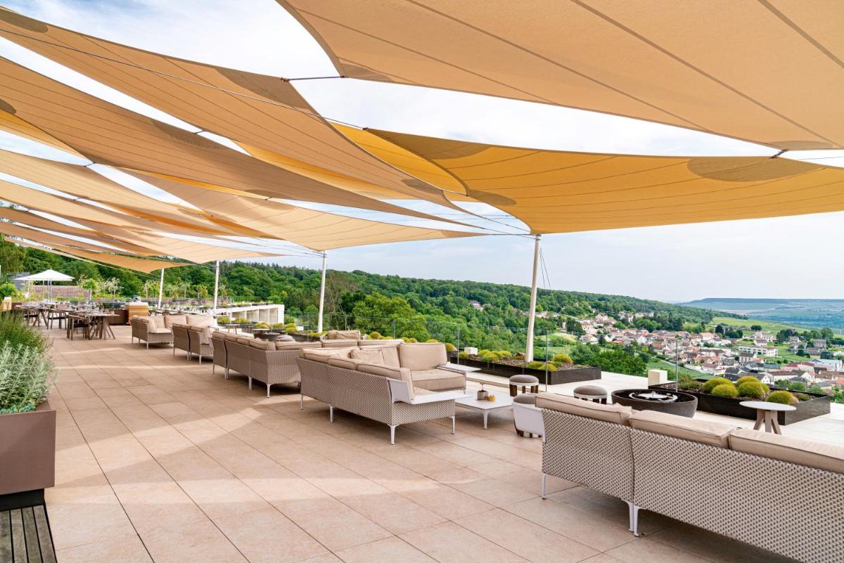 un patio avec des tables et des chaises sous un grand parasol dans l'établissement Royal Champagne Hotel & Spa, à Champillon