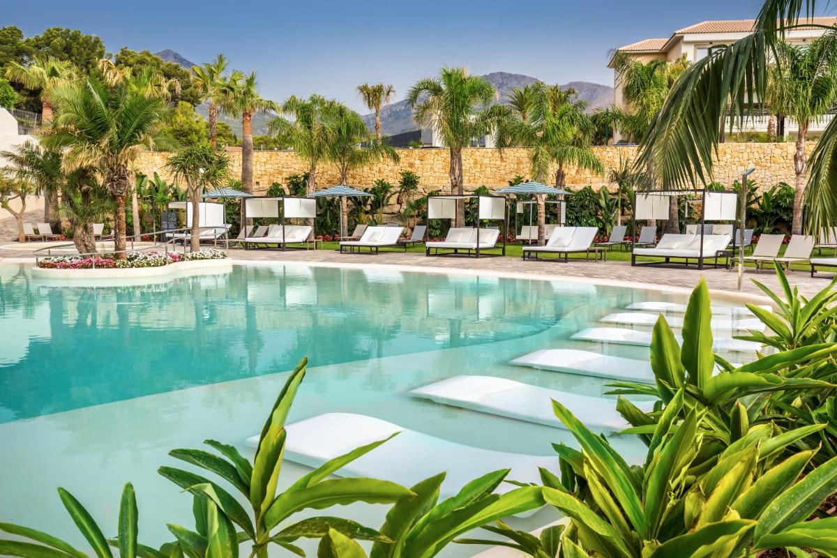 Una piscina en el resort con tumbonas y palmeras. en Barceló La Nucía Palms, en La Nucía