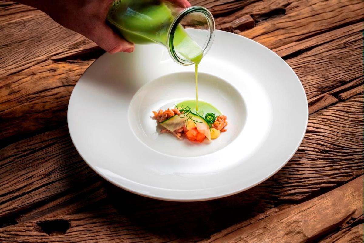 Eine Person schüttet Essen in einen weißen Teller. in der Unterkunft Relais & Châteaux Landhaus Stricker in Tinnum