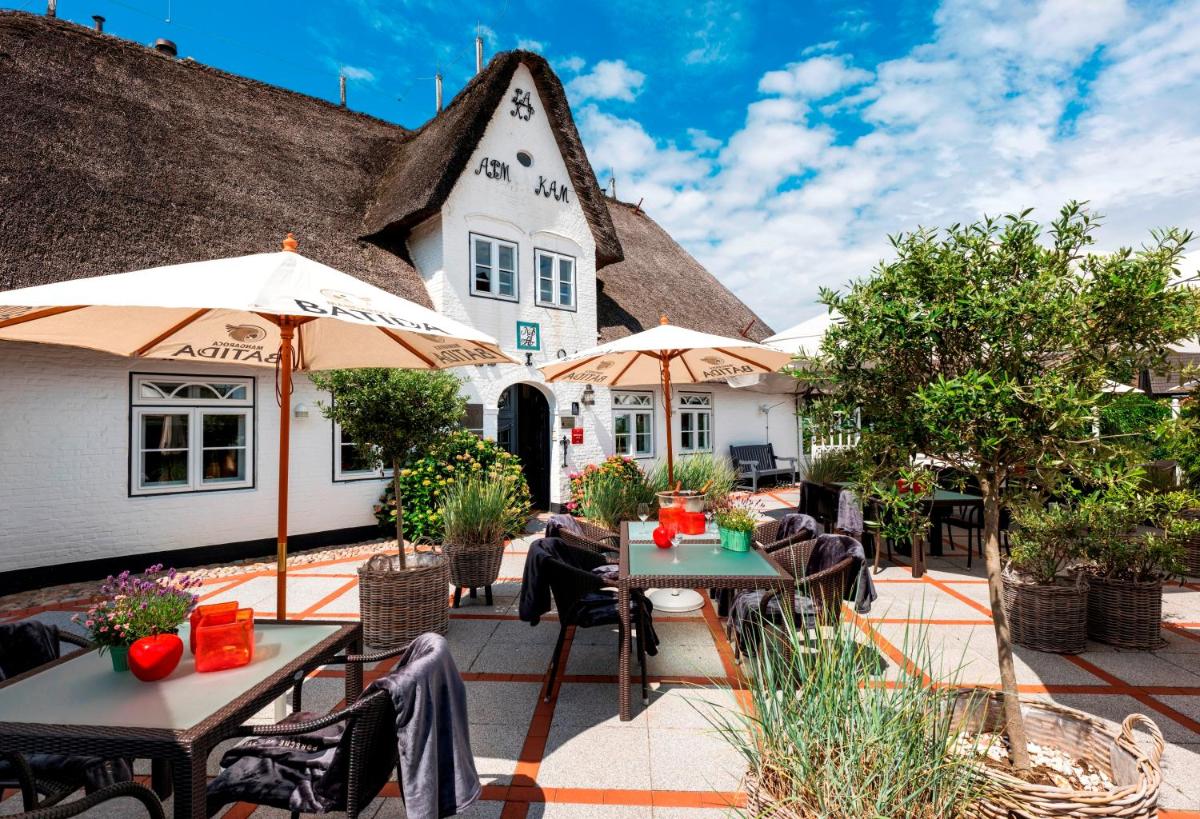 eine Terrasse mit Tischen und Sonnenschirmen vor einem Gebäude in der Unterkunft Relais & Châteaux Landhaus Stricker in Tinnum + 37 Fotos