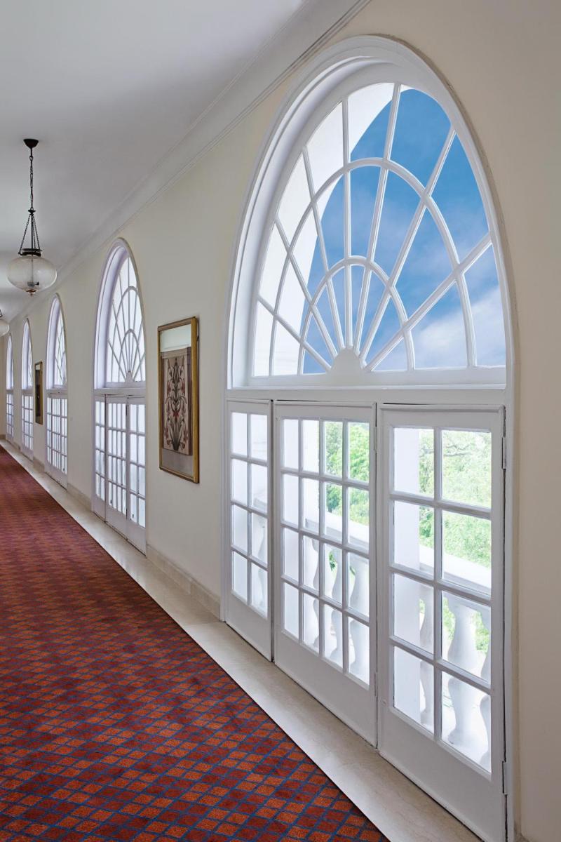 an empty hallway with large windows and a red carpet at Maidens Hotel New Delhi in New Delhi