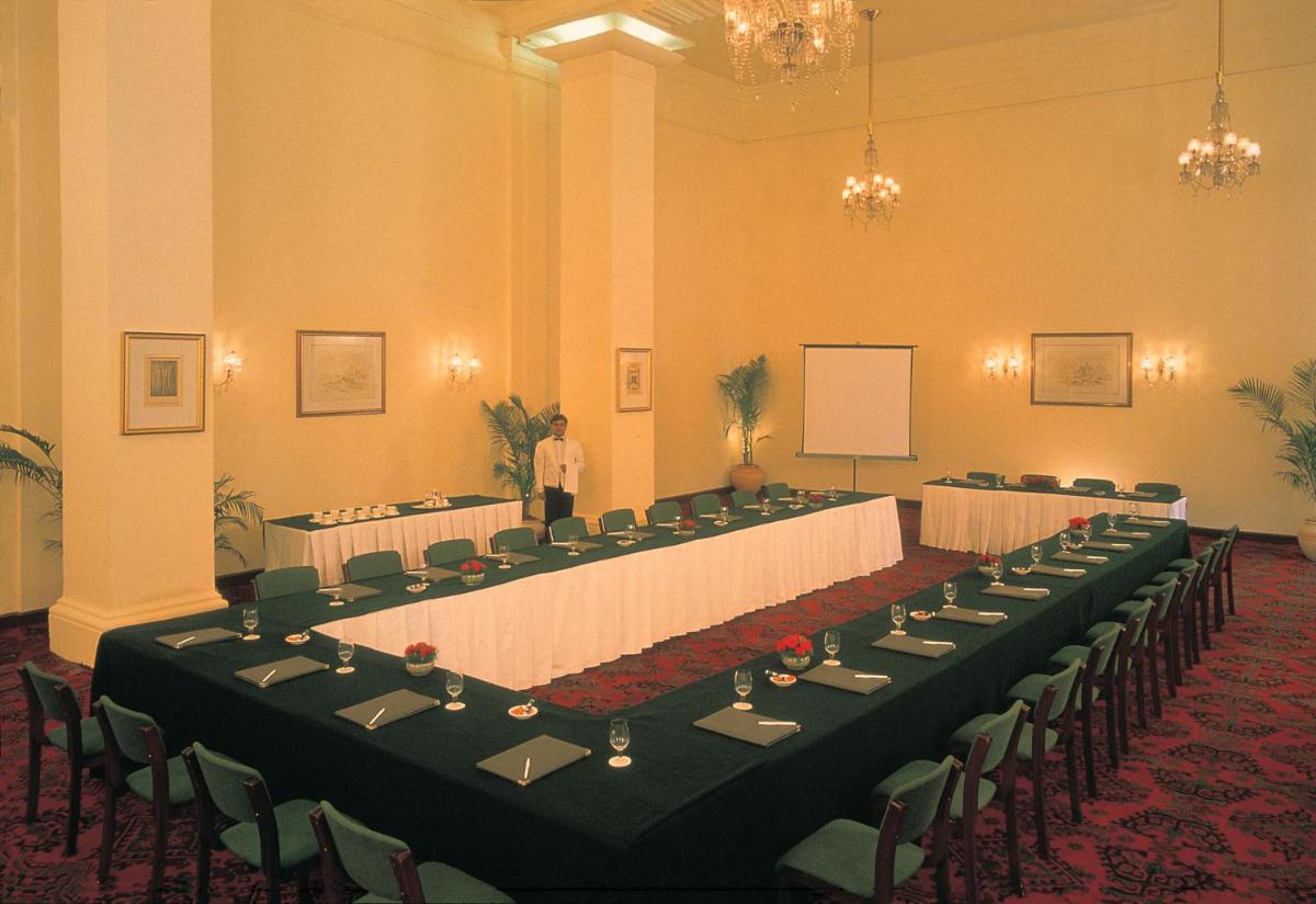 a man standing in a room with tables and chairs at Maidens Hotel New Delhi in New Delhi