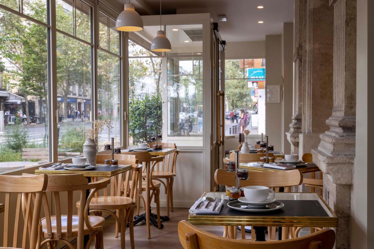 un restaurant avec des tables et des chaises en bois et des fenêtres dans l'établissement Le Petit Beaumarchais Hotel & Spa, à Paris