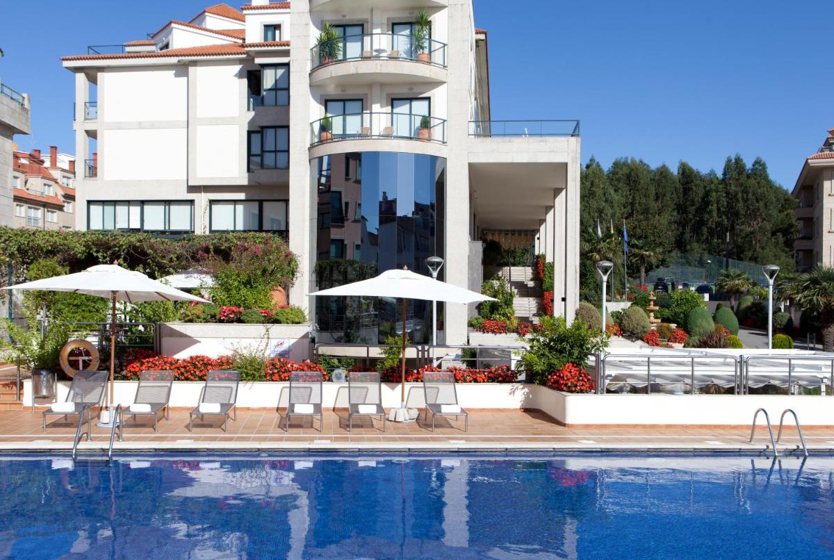Una piscina con sillas y sombrillas al lado de un edificio. en Hotel Carlos I Silgar, en Sanxenxo