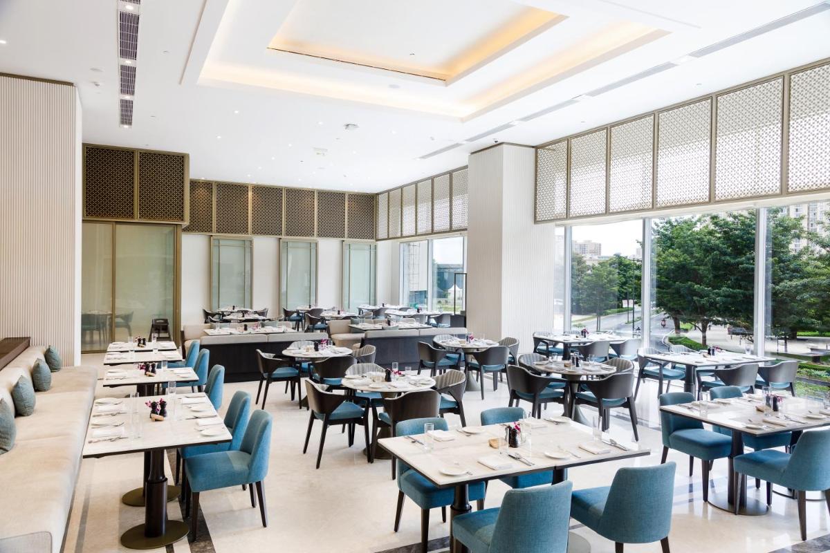 a restaurant with tables and chairs and large windows at The Leela Bhartiya City Bengaluru in Bengaluru a restaurant with tables and chairs and large windows at The Leela Bhartiya City Bengaluru in Bengaluru
