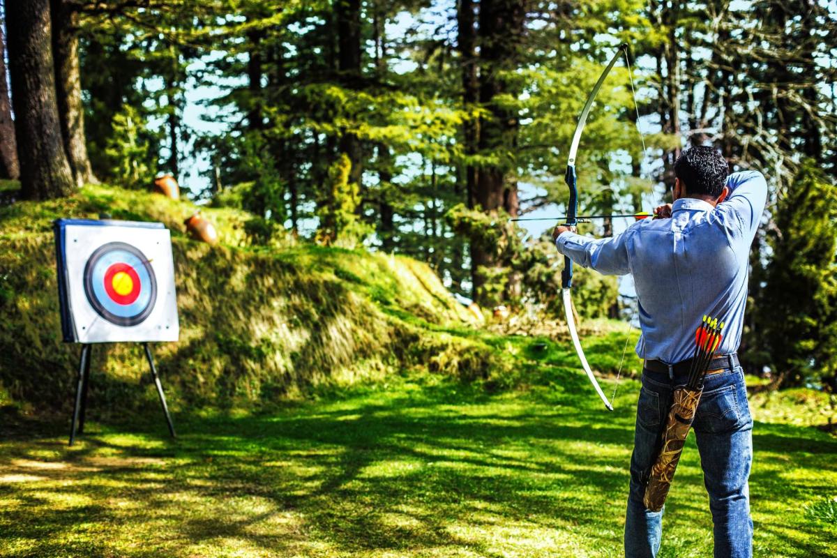 a man holding a bow and arrow next to a target at Wildflower Hall, An Oberoi Resort, Shimla in Shimla