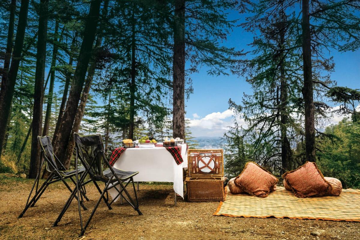 a table and chairs with a table and trees at Wildflower Hall, An Oberoi Resort, Shimla in Shimla