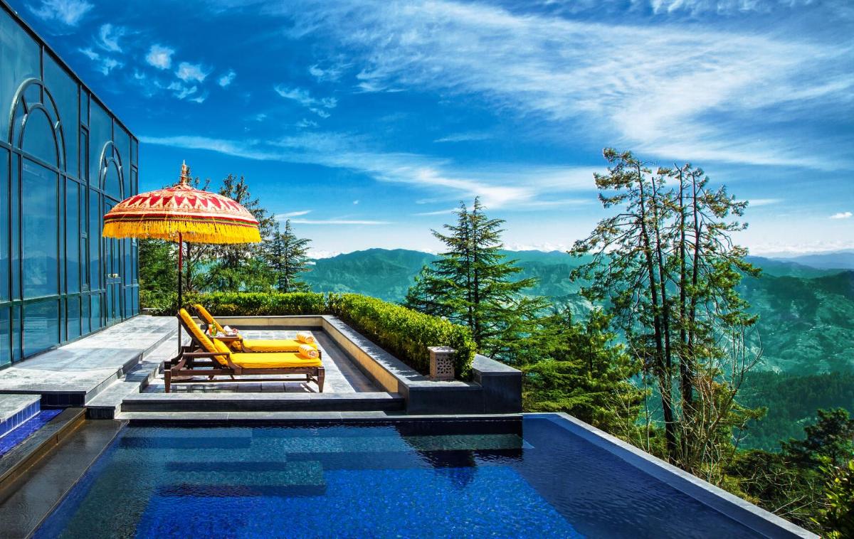 a swimming pool with an umbrella and chairs at Wildflower Hall, An Oberoi Resort, Shimla in Shimla