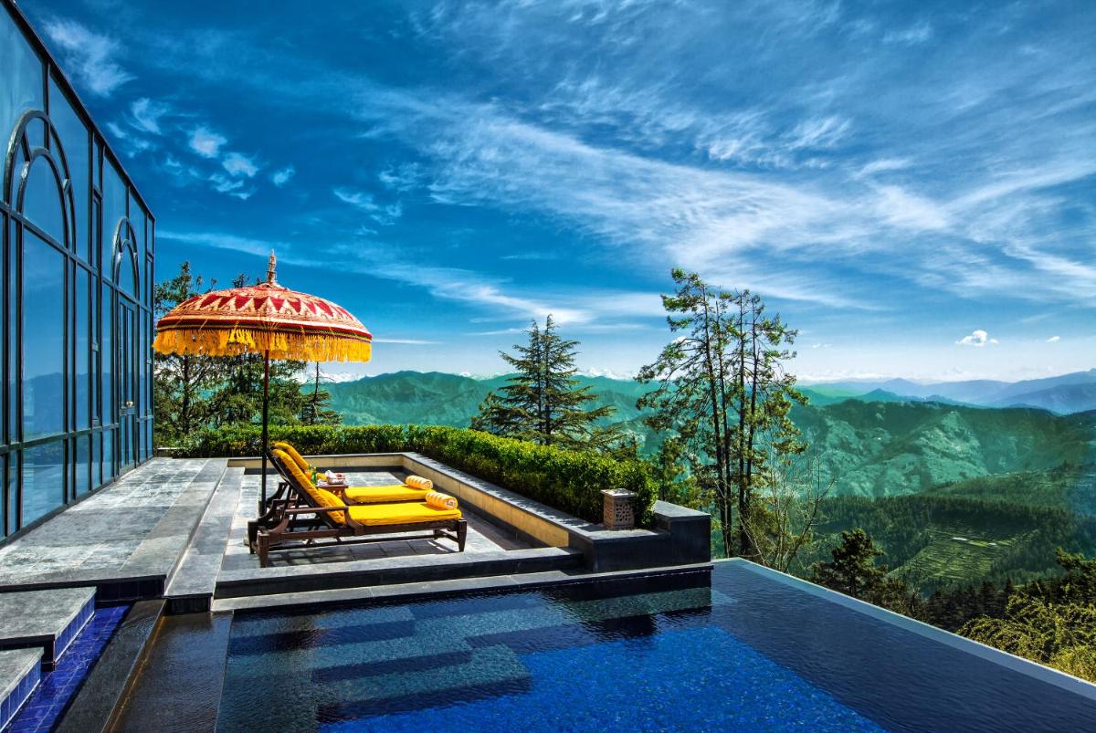 a pool with an umbrella and a chair at Wildflower Hall, An Oberoi Resort, Shimla in Shimla
