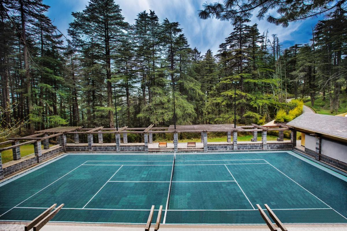 an indoor tennis court with trees in the background at Wildflower Hall, An Oberoi Resort, Shimla in Shimla