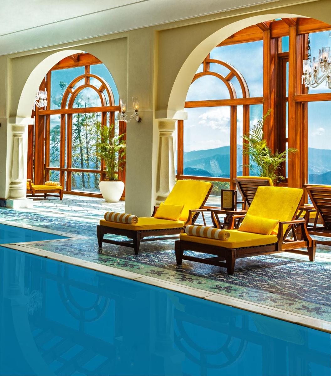 a hotel pool with yellow chairs and a swimming pool at Wildflower Hall, An Oberoi Resort, Shimla in Shimla