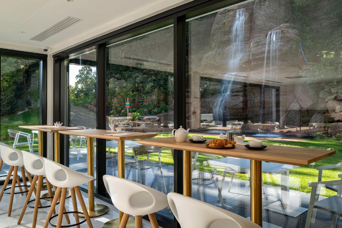 une salle à manger avec de grandes fenêtres, des tables et des chaises dans l'établissement 6717 Nature Hôtel & Spa Le Clos des Délices, à Ottrott