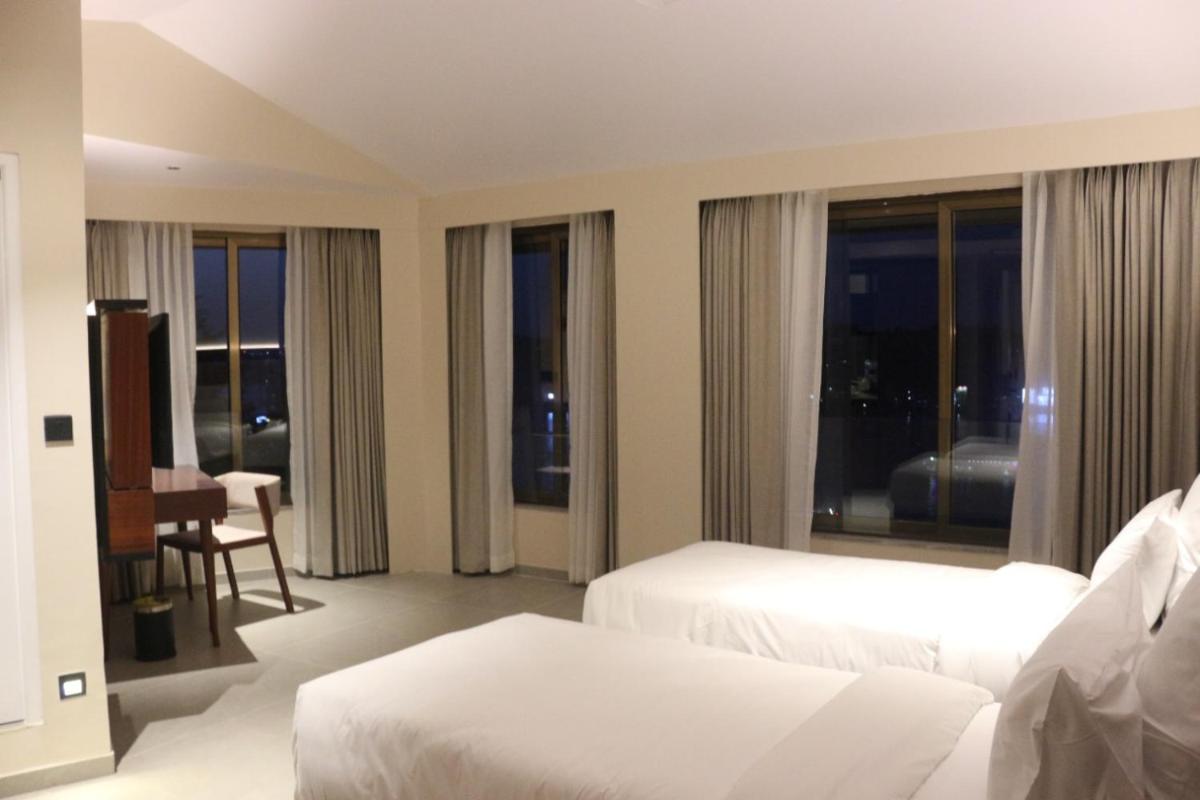 a hotel room with two beds and a desk and windows at The Crown Goa in Panaji